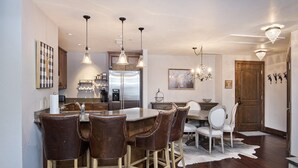 A modern kitchen with a central island, bar stools, pendant lighting, and a chandelier.