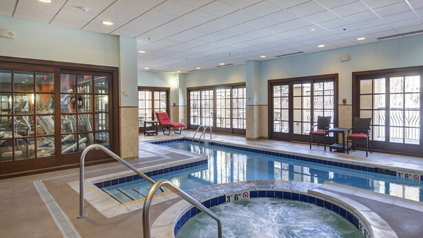 An indoor swimming pool with a hot tub, lounge chairs, and large windows.