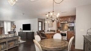 A spacious living room with a wooden dining table, comfortable chairs, a TV, and a chandelier.