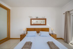 Hotellihuone, jossa on suuri sänky, kaksi yöpöytää, yölamppu, peili ja ikkuna, jossa on verhot.