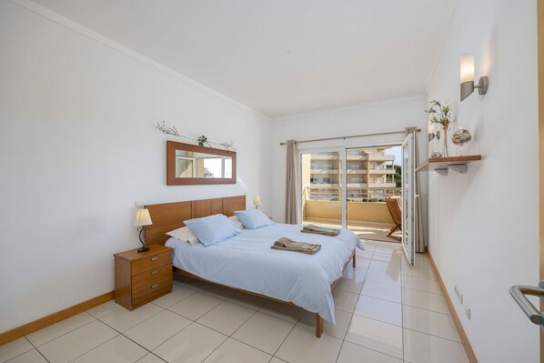A bedroom with a bed, bedside table, and a large window.