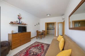 A living room with a sofa, TV, wooden cabinet, and a dining area with chairs and a table.