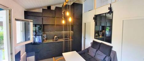 Ett kompakt bostadsutrymme med ett litet kök, en soffa, ett matbord och ett stort fönster.
