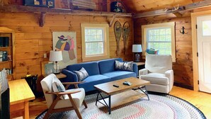 Interior acogedor de una cabaña de madera con un sofá azul, un sillón blanco, una mesa de centro de madera y un tapete estampado.