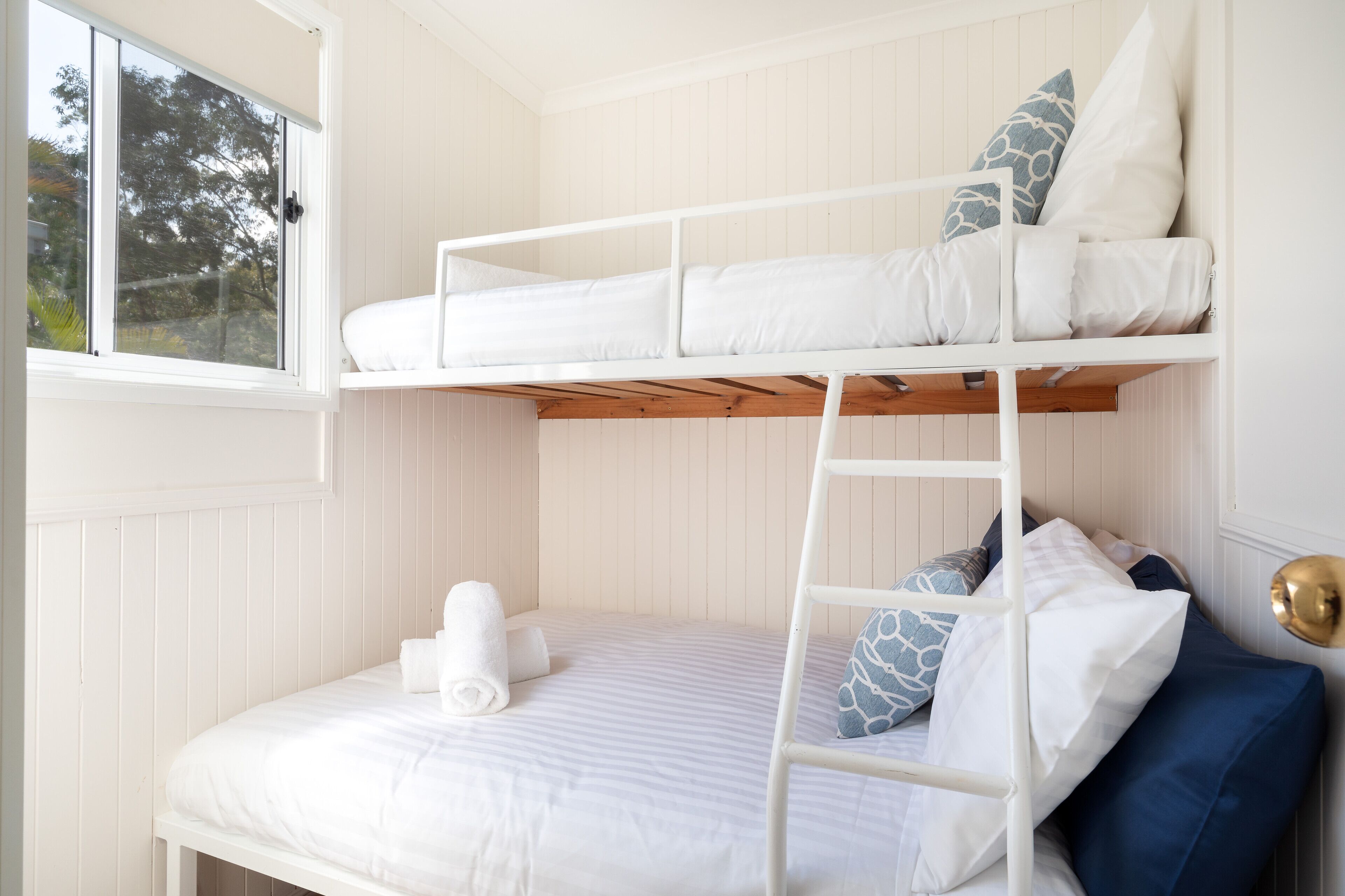 A bunk bed with a ladder, a window, and a door with a brass handle.