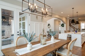 Un vaste espace dédié à la salle à manger, avec une table en bois, des chaises blanches et un lustre moderne.