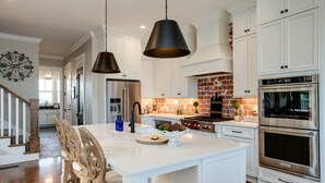 A modern kitchen with white cabinetry, a central island, a brick backsplash, and stainless steel appliances. - Gated Private Estate With Pool, Hilltop Views, and Game Room on 8 acres (Thompson's Station)