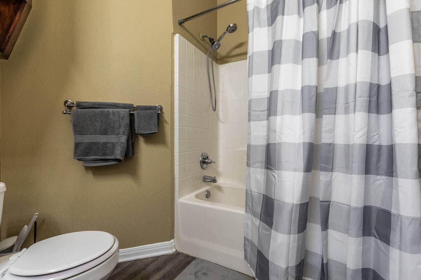 A bathroom with a toilet, a bathtub, and a shower. There are towels hanging on a rack.