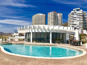 A modern hotel with a pool area, large windows, and a view of surrounding high-rise buildings.