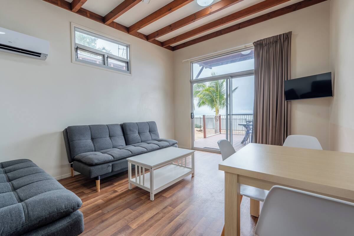 A modern living room with a sofa, a coffee table, a TV, and a balcony with a view.