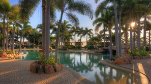 A resort pool area with palm trees, a clear pool, and a paved walkway. - Tasman Holiday Parks - Rollingstone (Rollingstone)