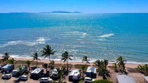 A beach with RVs parked on the sand, palm trees, and a view of the ocean. - Tasman Holiday Parks - Rollingstone (Rollingstone)