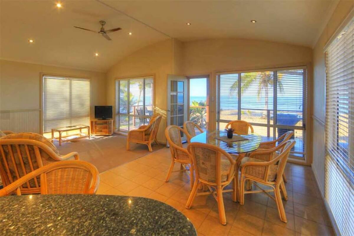 A spacious dining area with wicker furniture, a granite table, and large windows offering a view of the beach.