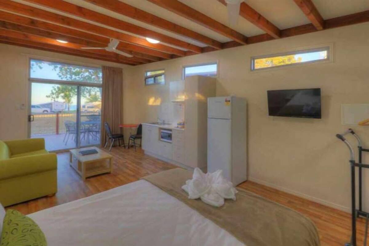 A room with a bed, a yellow armchair, a small table, a refrigerator, a TV, and a window.