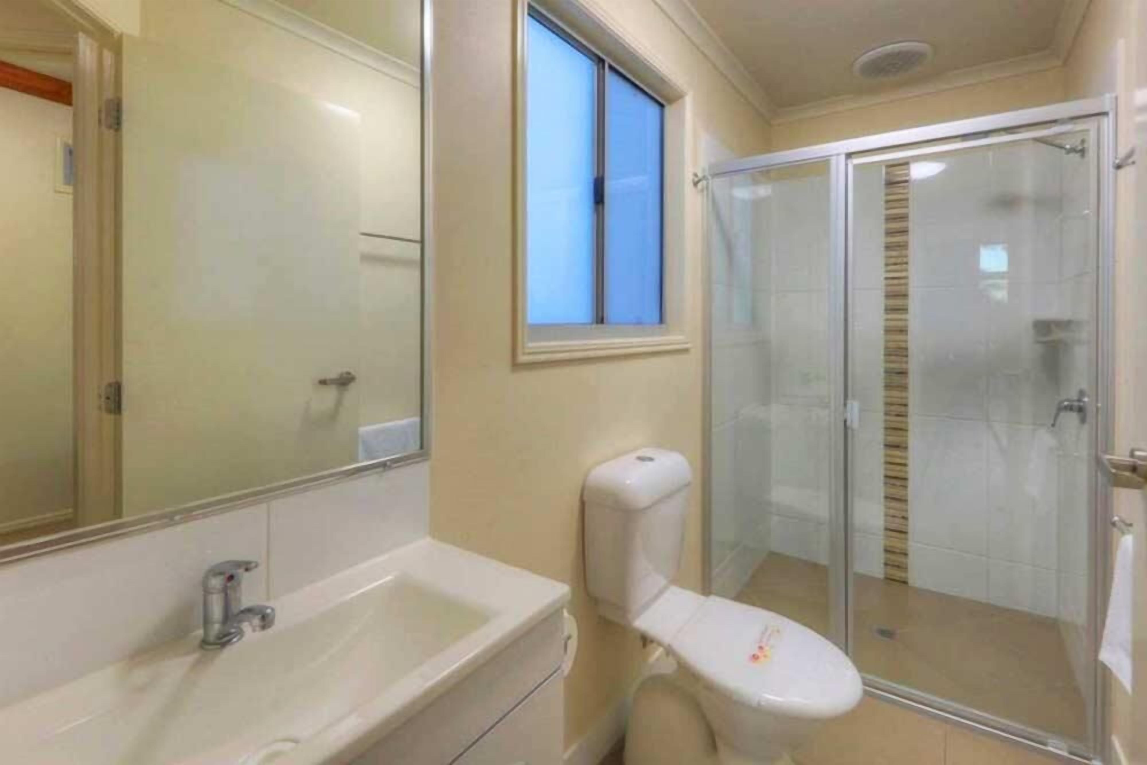 A bathroom with a glass shower enclosure, a toilet, and a sink.