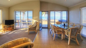A spacious living room with a television, wicker furniture, and large windows offering a view of the beach. - Tasman Holiday Parks - Rollingstone (Rollingstone)
