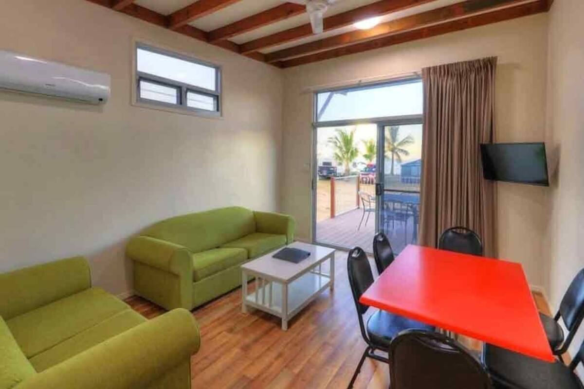 A room with a green sofa, a red table, and a TV mounted on the wall.