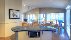 A kitchen with a built-in microwave, a dining area with wicker chairs, and large windows offering a view. - Tasman Holiday Parks - Rollingstone (Rollingstone)
