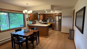 A modern kitchen with wooden cabinets, stainless steel appliances, and a large window offering a view of trees. - A Cozy Home Away From Home in Alaska! (Juneau)