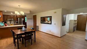 A modern kitchen with wooden cabinets, a stainless steel refrigerator, and a dining area with a wooden table and chairs. - A Cozy Home Away From Home in Alaska! (Juneau)