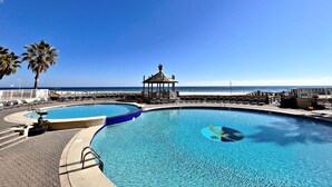 A pool with a gazebo, palm trees, and a beach view.