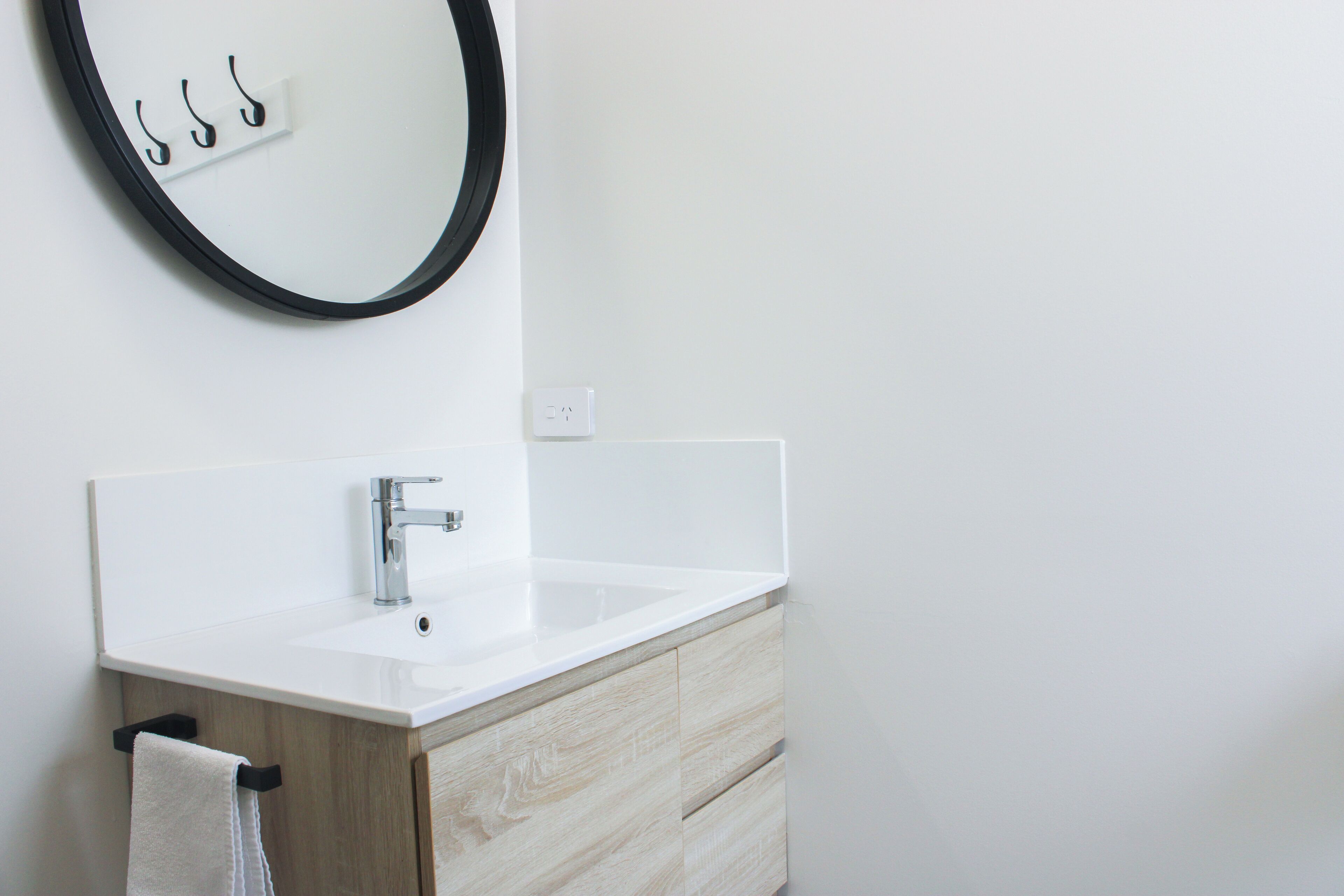 Une salle de bain moderne avec un lavabo blanc, un meuble en bois et un miroir rond doté de crochets.