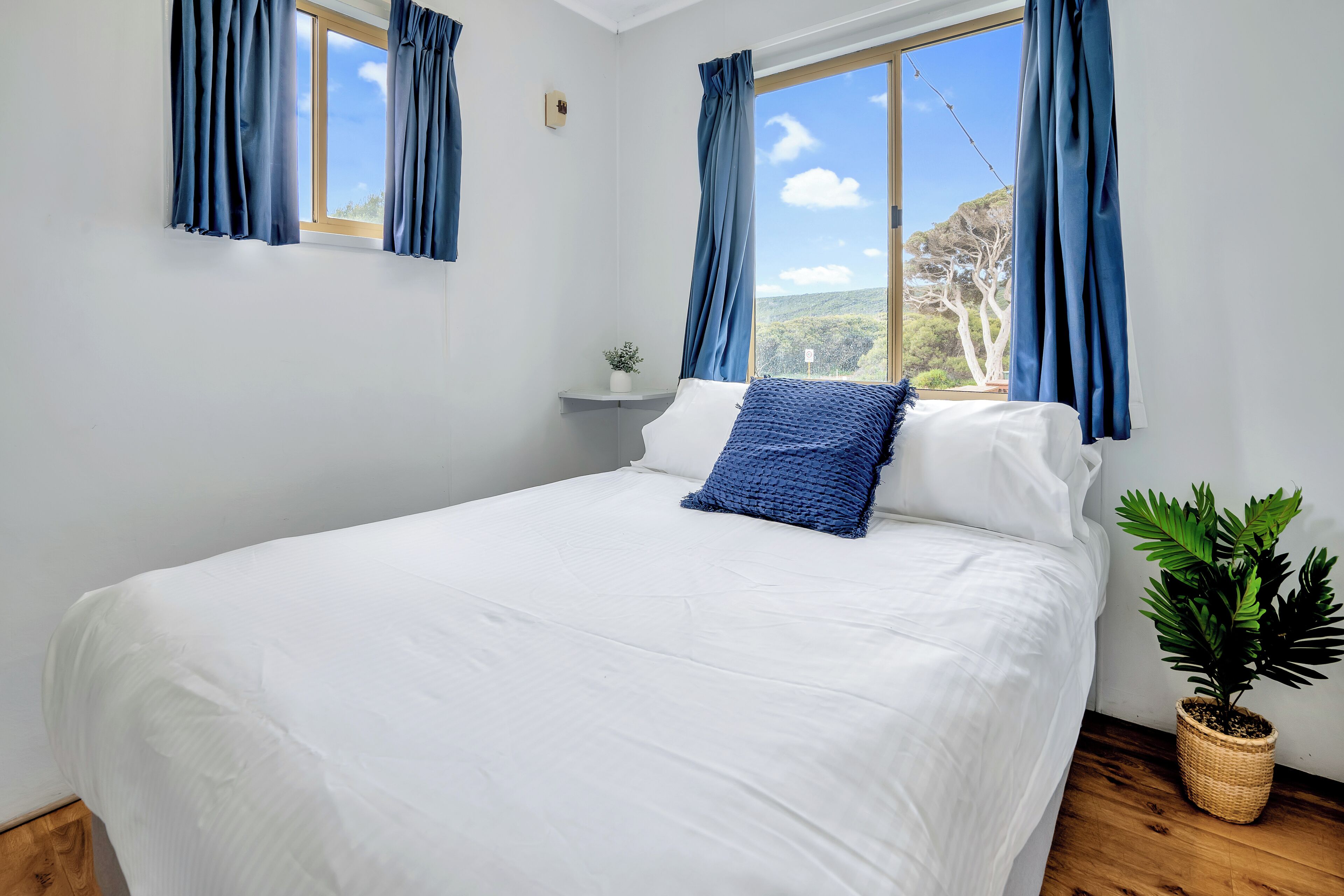 A bedroom with a large bed, white bedding, a blue pillow, and a potted plant.