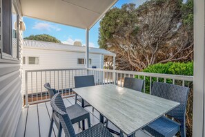 A covered outdoor patio with a table and chairs, a white building in the background, and trees. - Tasman Holiday Parks - Yallingup Beach (Yallingup)