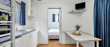 A compact hotel room with a kitchenette, a bed, a desk, and a TV.