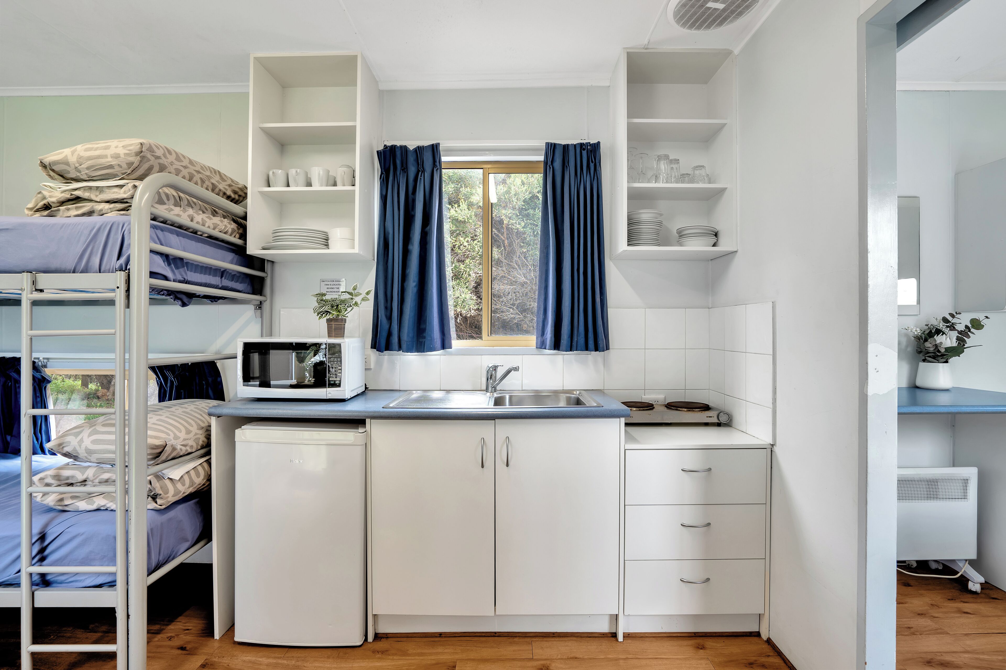 A compact room with a bunk bed, kitchenette, and a window with curtains.