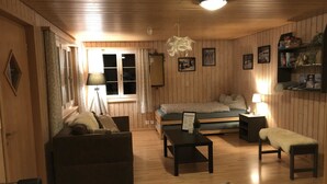 Ein gemütliches Zimmer mit Holzwänden, einer Couch, einem kleinen Tisch, einer Bank und einem Fenster mit Vorhängen.