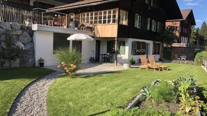 Ein zweistöckiges Haus mit Balkon, Steinmauer und gepflegtem Rasen.