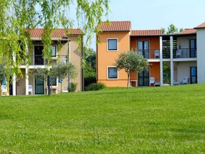 A multi-story residential building with balconies, a grassy lawn, and trees. - Holiday apartment with outdoor pool (Castelnuovo del Garda)