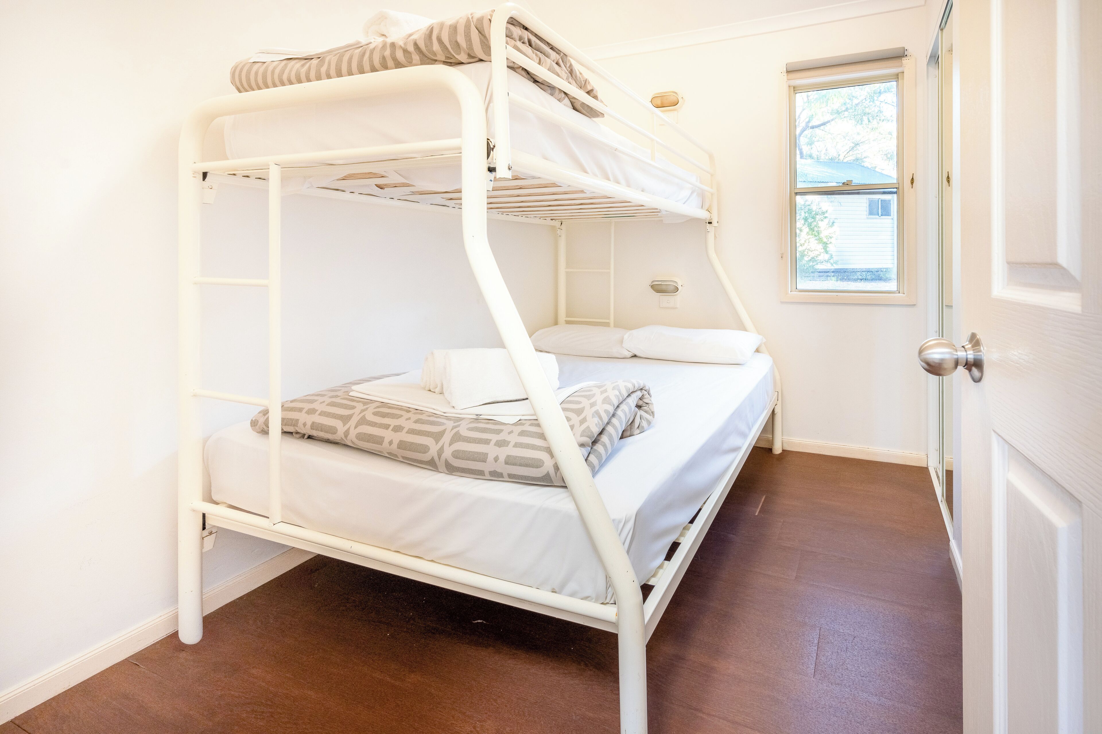 Una cama individual con ropa blanca y una ventana que da a una casa.