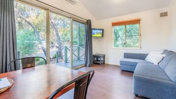 A spacious living area with a wooden dining table, a grey sofa, and a television mounted on the wall.