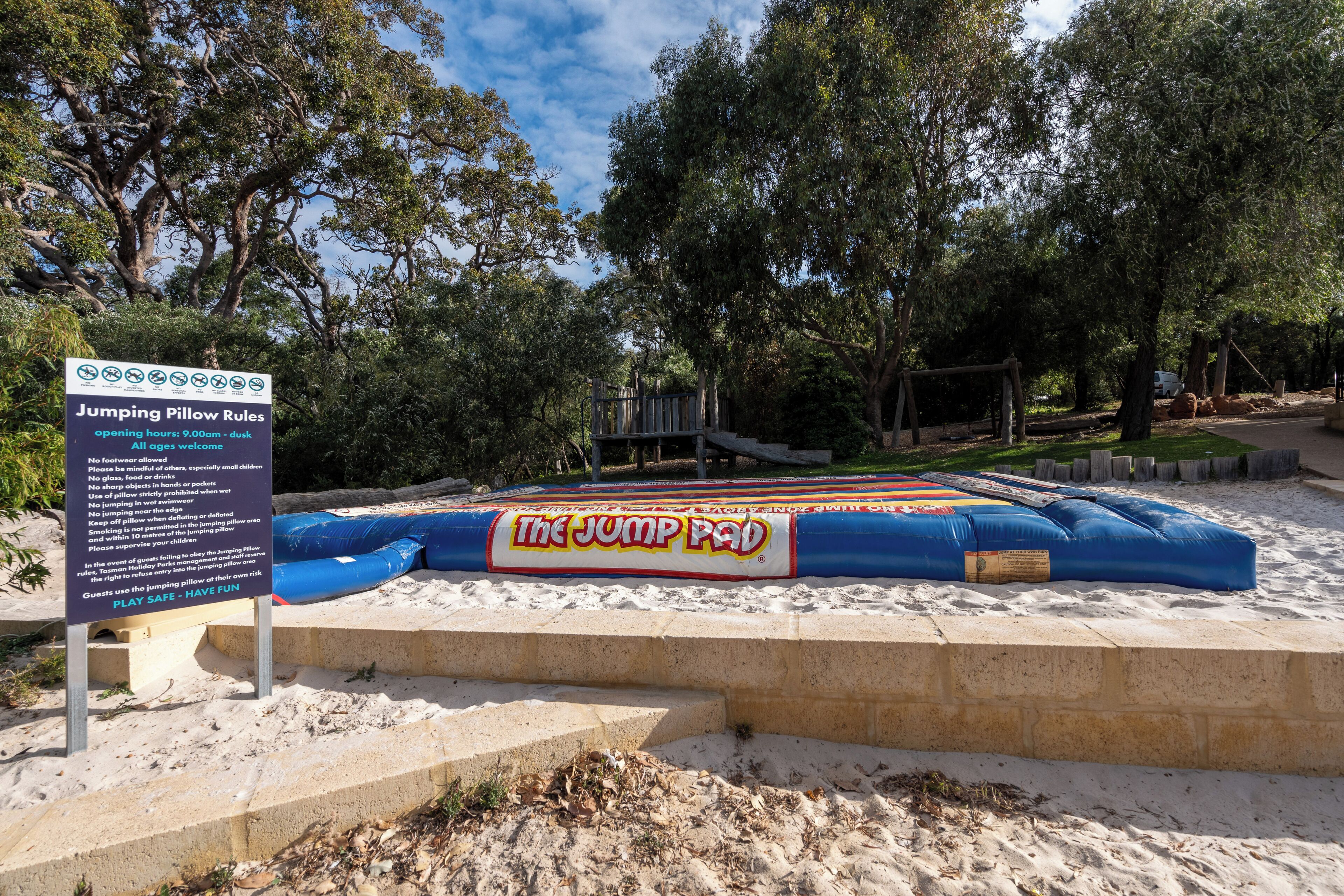 A jumping pillow with a sign detailing rules and opening hours.