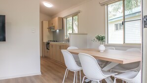 A modern kitchen with wooden cabinets, a white dining table, and four white chairs. - Tasman Holiday Parks - Yallingup Caves (Yallingup)