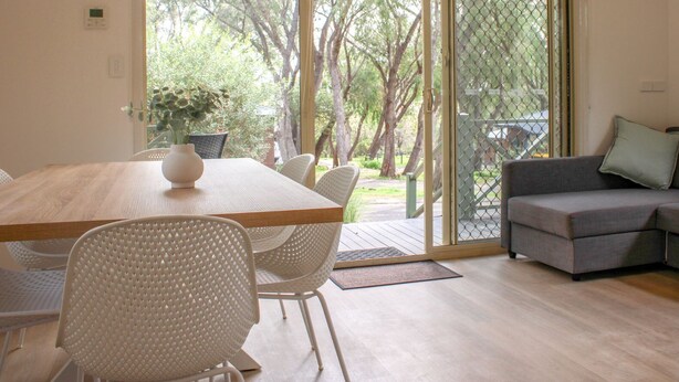 A modern living room with a wooden dining table, white chairs, and a grey sofa. - Tasman Holiday Parks - Yallingup Caves (Yallingup)