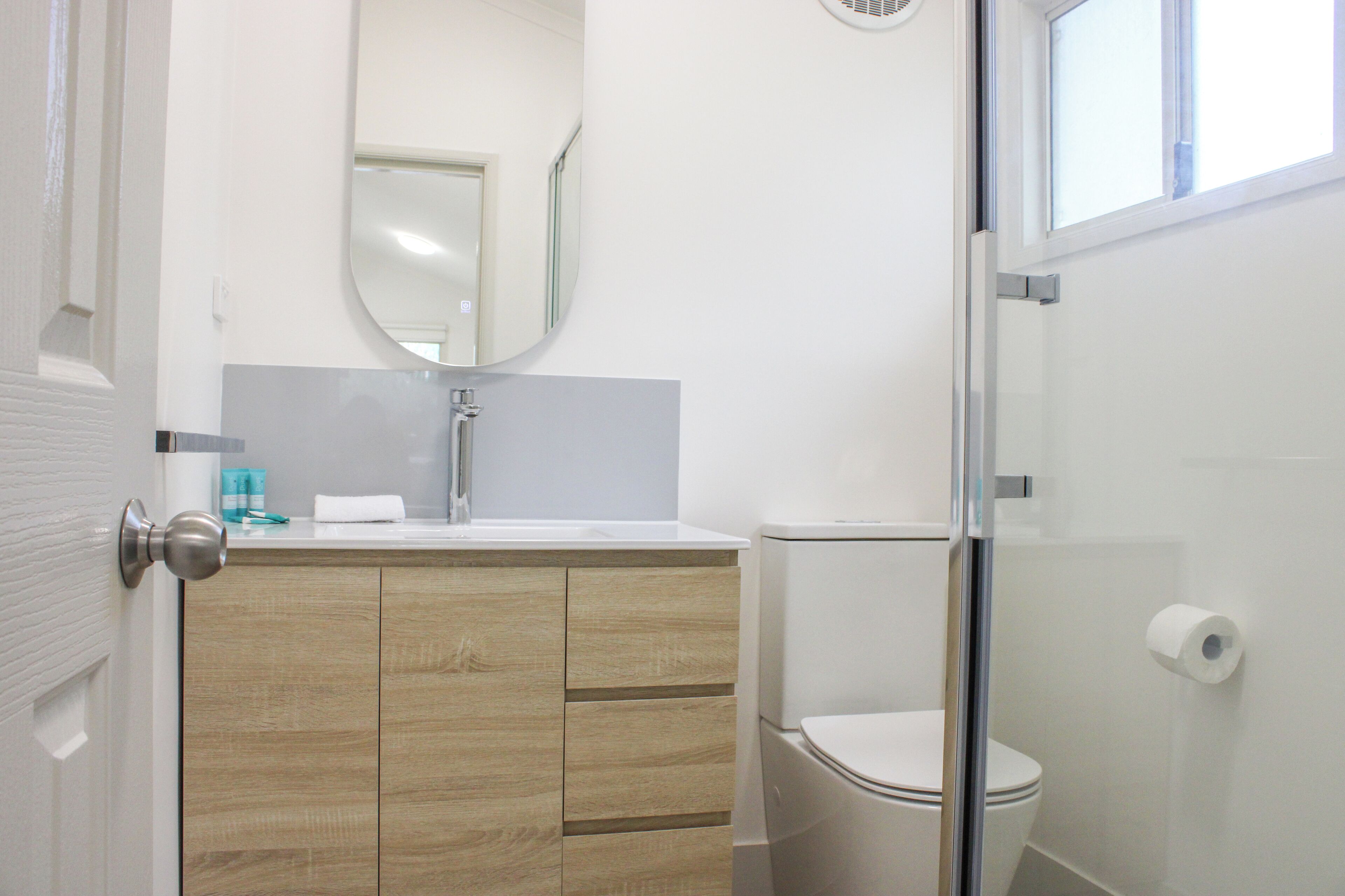 A bathroom with a wooden vanity, a toilet, and a glass shower enclosure.
