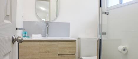 A bathroom with a wooden vanity, a toilet, and a glass shower enclosure.