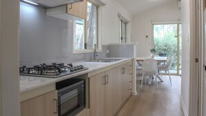 A modern kitchen with a gas stove, oven, and sink, wooden cabinets, and a dining area with a table and chairs. - Tasman Holiday Parks - Yallingup Caves (Yallingup)