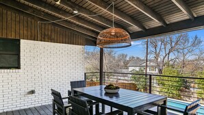 Eine überdachte Terrasse mit Tisch und Stühlen, einer hängenden Leuchte und Blick auf einen Swimmingpool sowie die umliegende Wohngegend.