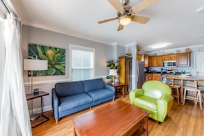 A living room with a blue sofa, a green armchair, a wooden coffee table, and a ceiling fan. - Modern condo with balcony, central AC, private washer/dryer - walk to beach (Tybee Island)