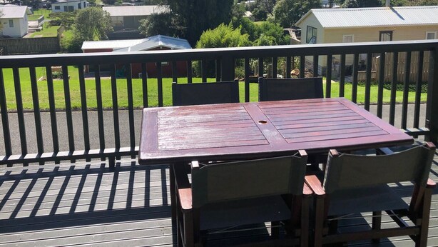 A wooden deck with a table and chairs, overlooking a residential area with houses and a body of water. - The Kakariki Cottage - Experience all that Aotea has to offer (Aotea, Kawhia)