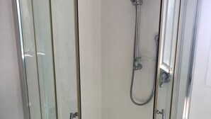 A glass-enclosed shower stall with a showerhead and handheld shower attachment. - The Kakariki Cottage - Experience all that Aotea has to offer (Aotea, Kawhia)