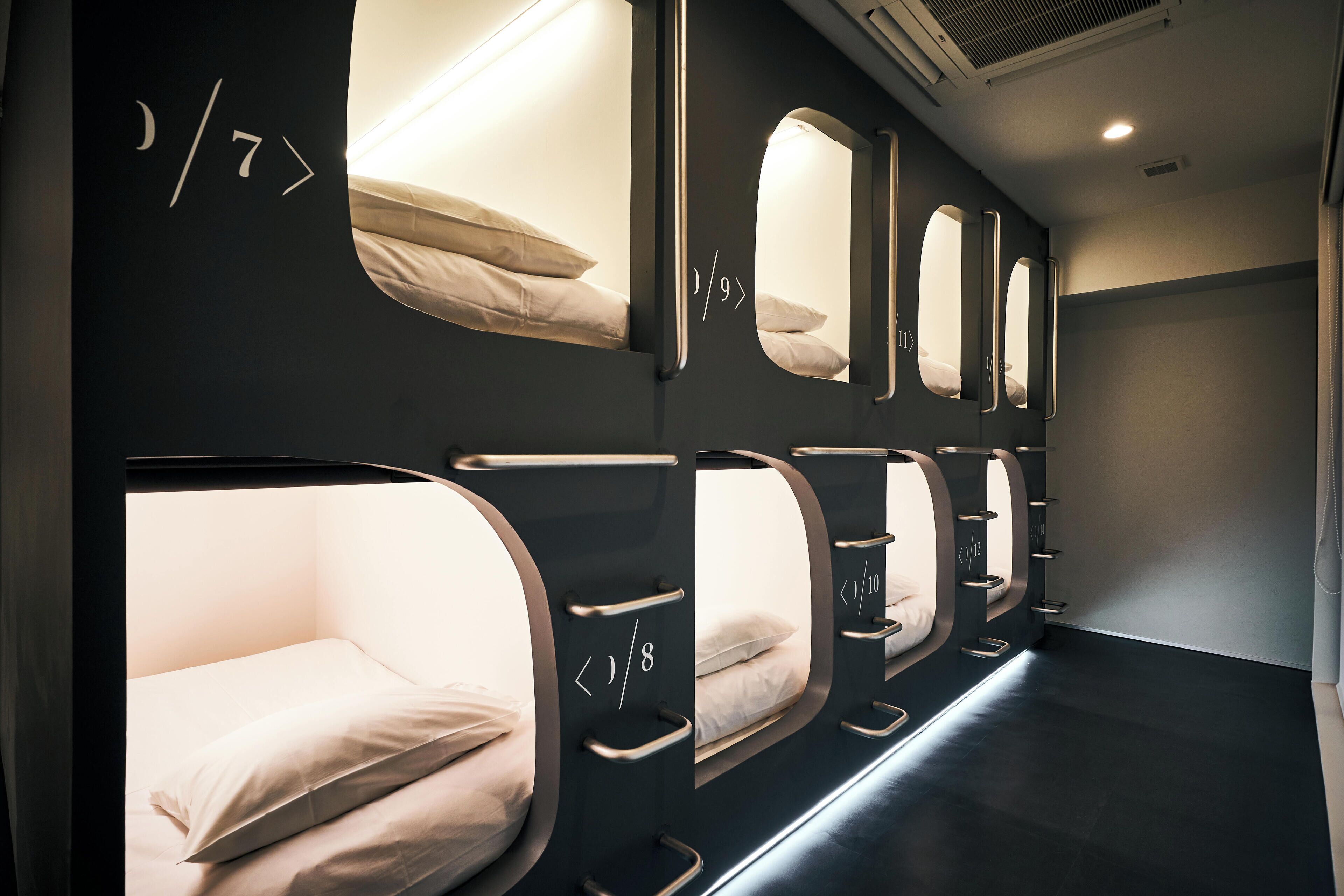 A row of private sleeping pods with individual beds, each pod has a small window and a mirror.