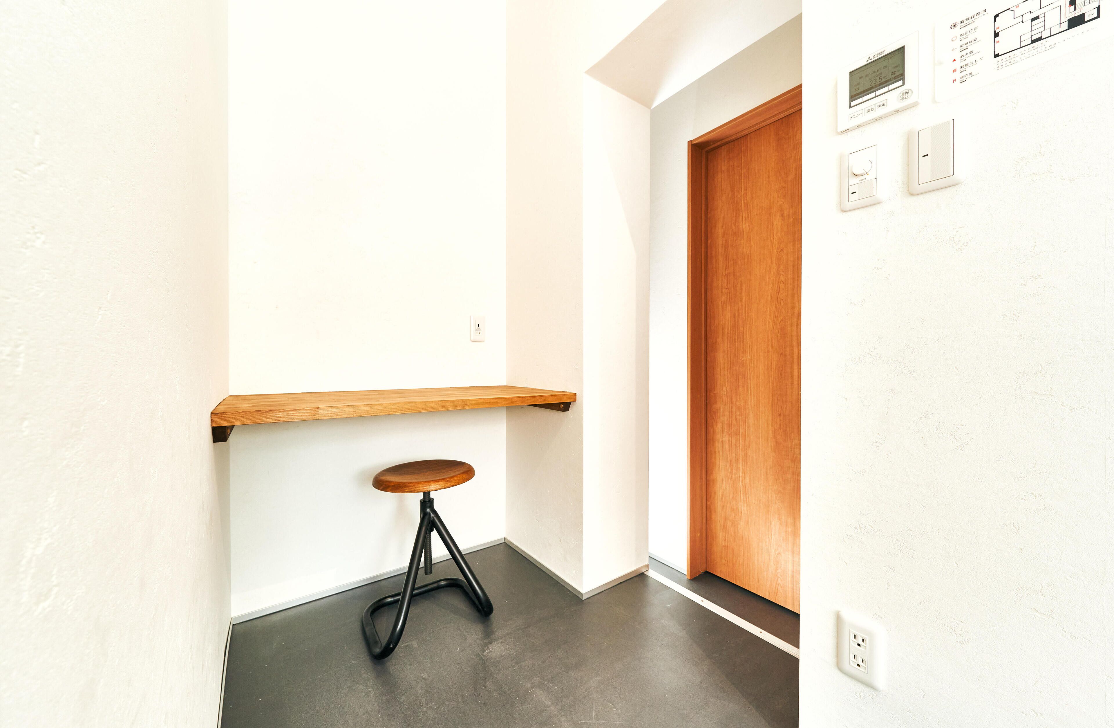 A hallway with a wooden door, a wall-mounted thermostat, and a small stool.
