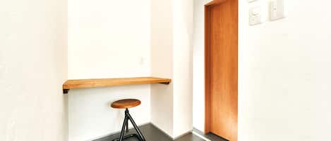 A hallway with a wooden door, a wall-mounted thermostat, and a small stool.