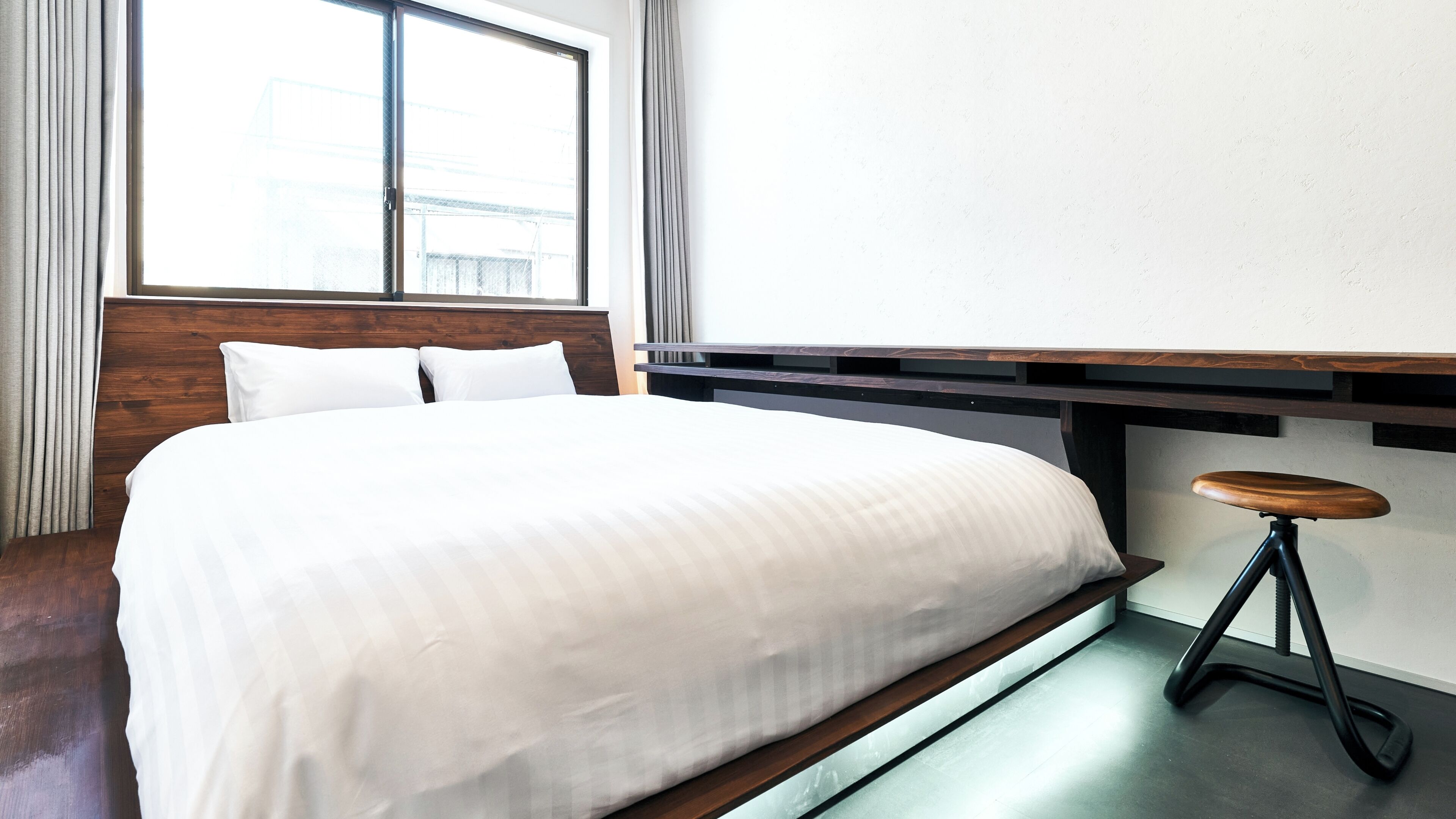 Habitación de hotel con cama, cabecera de madera, ventana, escritorio y taburete.