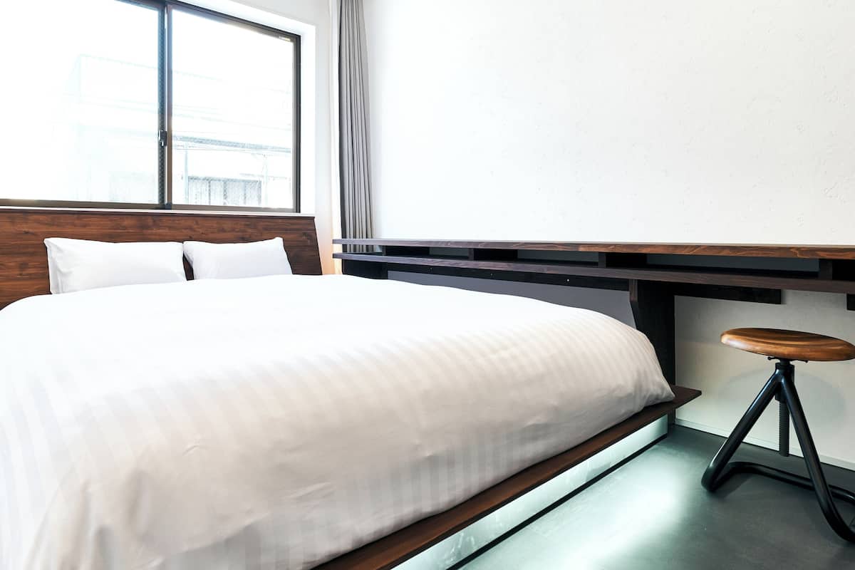 Habitación de hotel con cama, cabecera de madera, ventana, escritorio y taburete.
